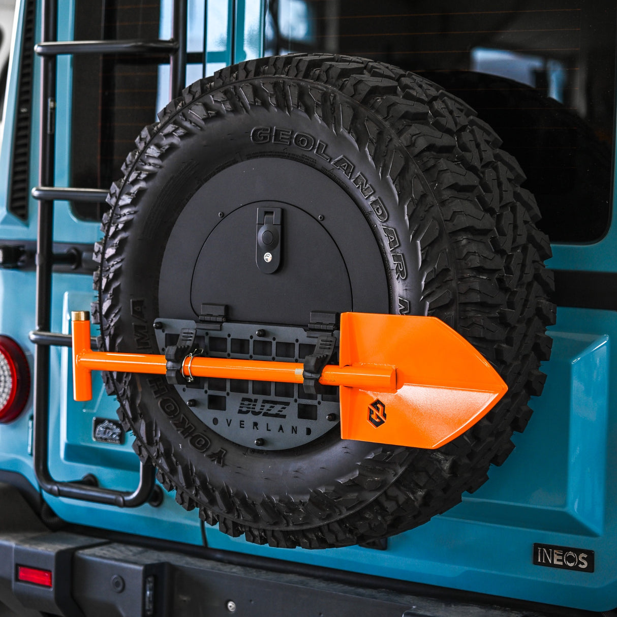 Tire carrier with a spare tire on a blue vehicle, featuring an orange tool.