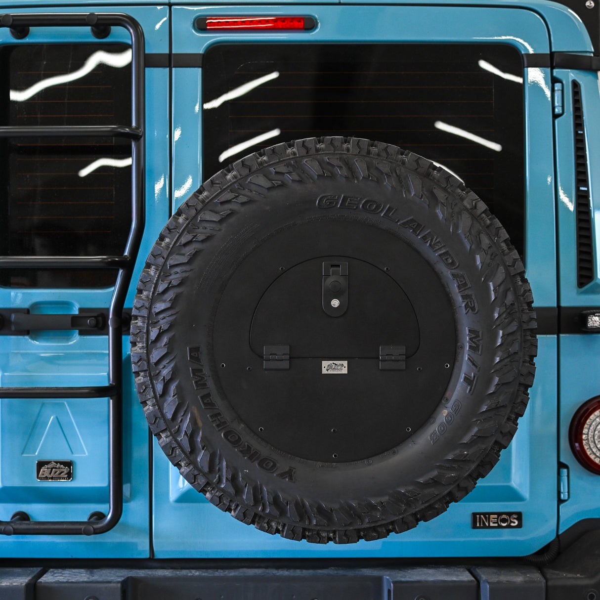 Buzz Overland Spare Wheel Storage Cubby for INEOS Grenadier, made from corrosion-resistant 5052 aluminium with a textured black powder coat, bolted to a 17-inch wheel for secure off-road storage.